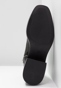 Semelle de botte en cuir noir avec talon et avant-pied texturés, affichant le numéro de taille 37 embossé près de la zone de la voûte plantaire.