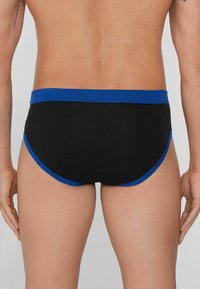 Schwarze Unterhosen mit einem blauen elastischen Bund und Besatz, die ein enges Design und eine glatte Stoffoberfläche aufweisen, mit Sicht von hinten.