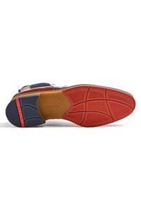 Semelle de chaussure en cuir marron présentant des accents en caoutchouc rouge et bleu, une surface texturée et un branding subtil sur la section beige.