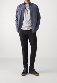 Blå skjorta med knappar över en grå t-shirt, parat med svarta byxor och svarta högklackade sneakers med gummisulor. Enkel halsband ingår.