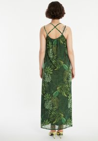 Maxi-Kleid aus grünem Stoff mit Blattmuster. Dünne, überkreuzte Träger und lockere Passform. Auffällige Rückendetails mit fließendem Fall.