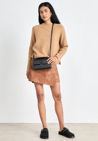 Suéter color camello, falda de cuero marrón y bolso bandolera negro con broche. Zapatos negros sin cordones con remaches decorativos. Diseño minimalista.