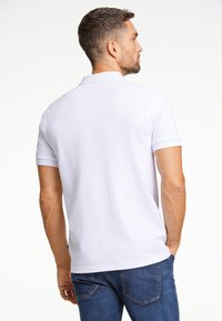 Valkoinen polo paita perinteisellä muotoilulla, lyhyillä hihalla ja kauluksella. Kangas näyttää sileältä ja kevyeltä. Yhdistetty sinisiin farkkuihin.