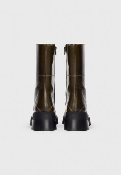 Stivali ankle in pelle marrone con una finitura liscia, cerniere laterali e suole nere spesse. Presentano cuciture a contrasto e un design strutturato.