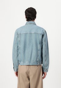 Gai zila denim jaka ar klasisku dizainu, ar norādītu apkakli, aizmugures šuvēm un pogātām piedurknēm.