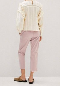 Top ligero de crema con mangas acampanadas, combinado con pantalones cortos rosa claro. La modelo lleva zapatos marrones sin cordones con suela negra.