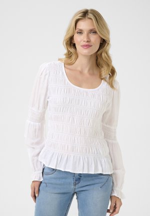 Weiße Bluse aus gerafftem, strukturiertem Stoff, mit langen Ärmeln und Rüschensaum. Kombiniert mit hellblauen Jeans. Einfaches, lässiges Design.