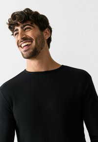 Black long-sleeve shirt with a round neckline, crafted from textured fabric, shown on a smiling male model against a plain background.