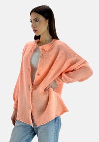 Cardigan button-down oversize in morbido e leggero maglione pesca chiaro. Presenta un colletto rotondo, polsini a costine e tre bottoni color oro.