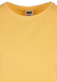 Žluté bavlněné tričko s kulatým výstřihem, krátkými rukávy a hladkým povrchem. Na štítku je nápis "URBAN CLASSICS" a velikost XS.