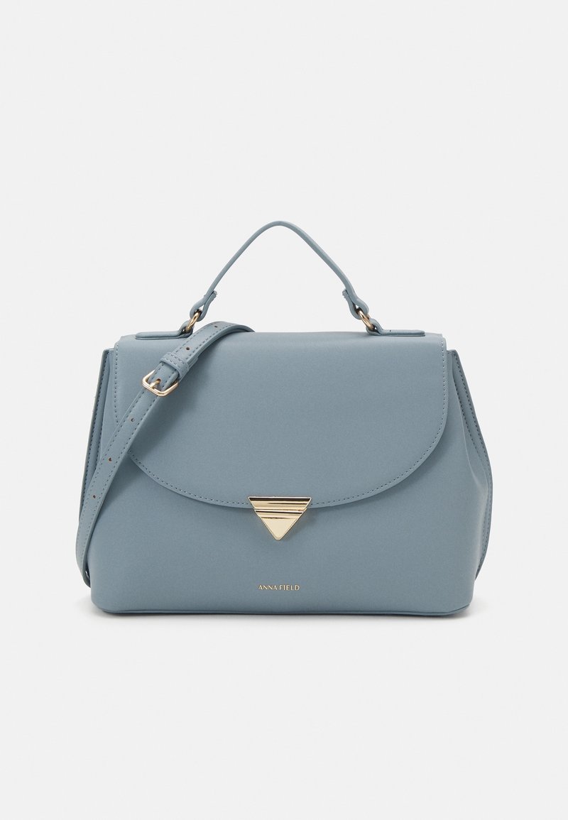 Bolso estructurado de color azul claro, hecho de material suave, con una tapa frontal que presenta un acento triangular dorado y una correa desmontable.