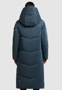 Lange donkergroene pufferjas met een hoge kraag en capuchon, voorzien van chevronstiksels en een logo aan de zijkant. Glad, glanzend textuur.