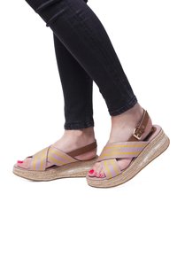 Noge v wedges sandalu s svetlo rjavimi in vijoličnimi križnimi trakovi, z zlatim zaponko in rožnato manikuro nohtov, v kombinaciji s črnimi oprijetimi jeans.