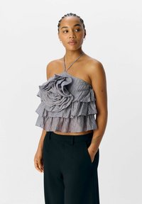 Grijze gelaagde crop top met drie ruches, met een bloemenaccent in het midden. Gemaakt van textiel met een structuur. Halternek ontwerp.