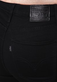 Jeans de mezclilla negra con una etiqueta de cuero de Levi's en la parte posterior de la cintura. Presenta bolsillos traseros estándar con un diseño de costura sutil.