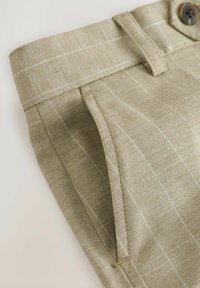 Pantaloni beige chiaro con texture in lino, caratterizzati da un sottile motivo a righe bianche, una vita cucita e un unico bottone marrone.