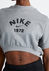 Felpa grigia corta con scollo rotondo, con il logo Nike e "1972" in nero sul davanti. Tessuto morbido e strutturato.