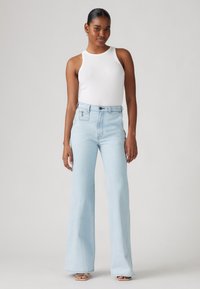 Világoskék, bővülő farmernadrág magas derékkal, denim anyagból készült. Fehér, testhezálló toppal párosítva. Sima textúra, minimális részletezés.