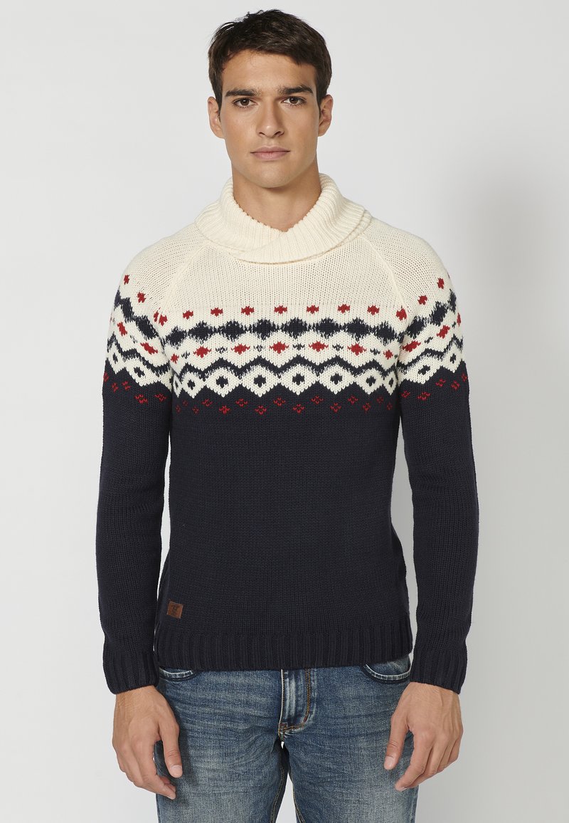 Suéter de punto con cuello alto en color crema, cuerpo en azul marino y patrón Fair Isle con acentos en rojo y azul. Puños y dobladillo acanalados.