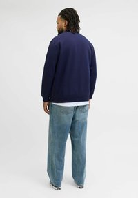 Sudadera azul marino de corte relajado, con puños y dobladillo de canalé, combinada con jeans de pernera ancha en azul claro. Camiseta blanca lisa visible por debajo.