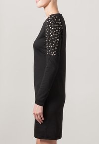 Robe noire à manches longues, ajustée. Caractéristiques : épaules ornées de clous métalliques et d'accents texturés. Finition en tissu lisse.