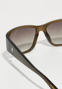 Sunglasses featuring a brown gradient lens, thick frame, and slightly curved temple arms with a glossy finish and logo detail on the side.