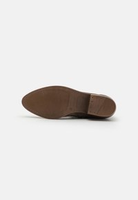 Suela de zapato de cuero marrón con una superficie lisa, patr�ón de estrías y un logo incrustado. La forma es redonda en la punta con un tacón plano.