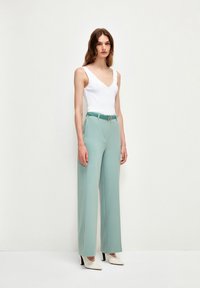 Světle modré kalhoty širokého střihu s hladkým povrchem, doplněné o odpovídající opasek a bílý přiléhavý top. Oblečení doplňují špičaté podpatky.