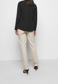 Blusa negra de manga larga con una costura en la parte posterior, combinada con pantalones ajustados beige claro y zapatos de tacón negros.