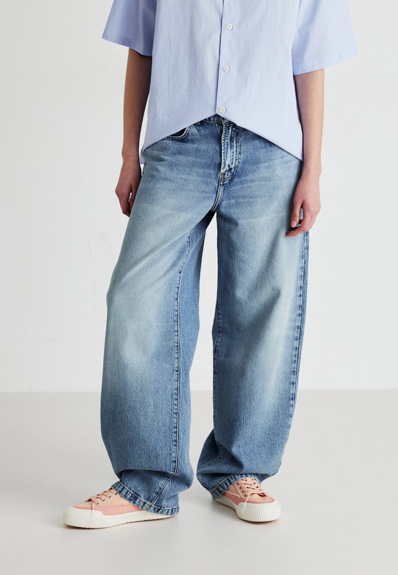 Light blue oversized jeans with a straight leg design and faded texture, paired with pastel pink sneakers featuring white soles.