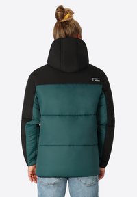 Gewatteerde jack met een zwarte capuchon en bovenkant, en een teal onderste gedeelte. Bevat een opvallende textuur en een logo label op de achterkant.