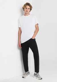 T-shirt bianco a collo rotondo, jeans neri slim-fit e sneakers grigie con accenti bianchi, neri e grigi. Stile e vestibilità casual moderna.