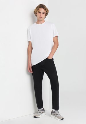 T-shirt bianco a collo rotondo, jeans neri slim-fit e sneakers grigie con accenti bianchi, neri e grigi. Stile e vestibilità casual moderna.
