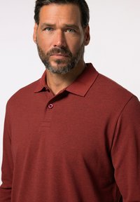 Langärmliges Polo-Shirt aus dunkelrotem Stoff mit strukturiertem Finish. Verfügt über einen Kragen und eine Knopfleiste mit einem rosa Knopf-Akzent.