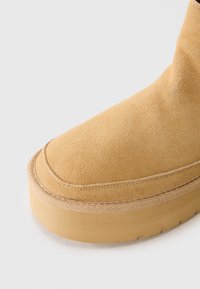 Botte en suede marron clair avec une semelle épaisse et des coutures visibles sur le bout et autour de la base, sur fond blanc.