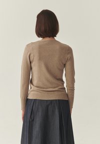Pull beige à manches longues avec un col arrondi, associé à une jupe plissée bleu profond. Les textures sont lisses et douces.