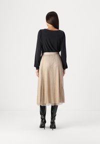 Čierny top s dlhým rukávom a záhybmi na chrbte, skombinovaný s lesklou zlatou midi sukňou a čiernymi čižmami po kolená, vytvára kontrastný outfit.