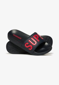 Des sandales noires à glissière avec une large sangle affichant le texte rouge en relief "SUPREME". Semelle noire texturée. Matériau synthétique lisse.