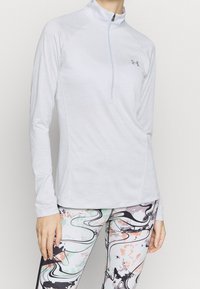 Vaaleanharmaa pitkähiha urheilupaita, jossa on puolivetoketjullinen kaulus ja sileä kangas, yhdistetty värikkäisiin, abstraktikuosisiin leggingseihin.