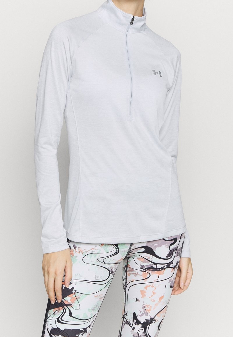 Vaaleanharmaa pitkähiha urheilupaita, jossa on puolivetoketjullinen kaulus ja sileä kangas, yhdistetty värikkäisiin, abstraktikuosisiin leggingseihin.