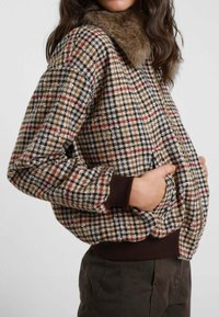 Giacca a motivo houndstooth marrone con colletto in pelliccia sintetica, polsini a coste e tasche laterali. Forma ampia e texture morbida.