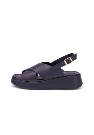 Czarna sandałka na platformie z szerokimi, skrzyżowanymi paskami ze skóry i regulowanym paskiem wokół kostki z złotą klamrą na białym tle.