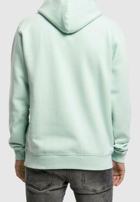 Felpa verde menta realizzata in materiale morbido, con tasca a marsupio e cappuccio regolabile con cordino, abbinata a pantaloni grigi.
