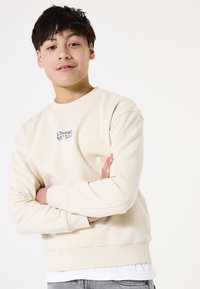Sudadera beige claro con cuello redondo, mangas largas, puños y dobladillo de canalé. Presenta un diseño de texto azul que dice "Choose" en la parte delantera.