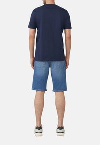 Marineblauwe katoenen T-shirt gecombineerd met lichtblauwe denim shorts, met een ontspannen pasvorm en bijpassende sneakers. Casual ontwerp met strakke lijnen.