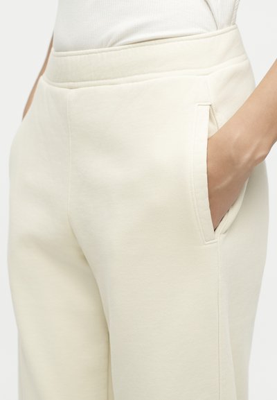 Κοντινό πλάνο ατόμου που φοράει εκρού παντελόνια με το χέρι στην πλαϊνή τσέπη, τονίζοντας την υφή του υφάσματος και το σχέδιο της τσέπης.