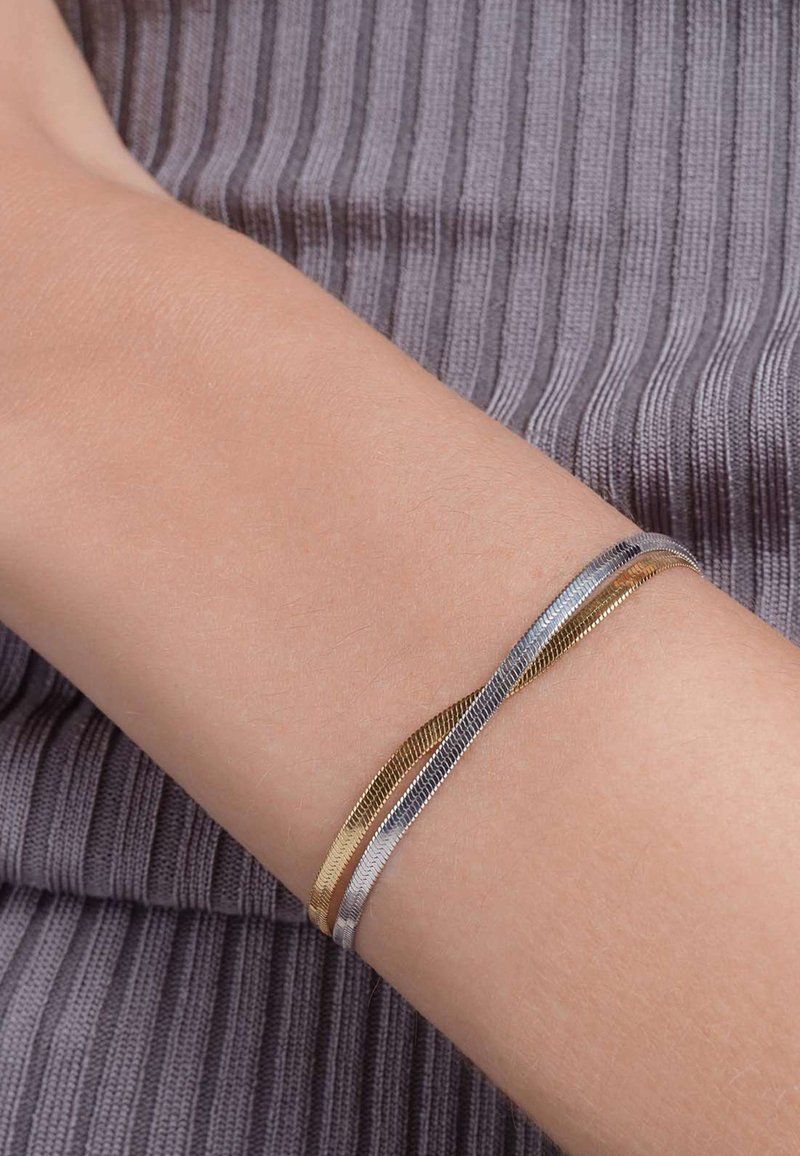 Bracciale a strati in oro e argento con filamenti testurizzati, caratterizzato da un design flessibile che si adatta al polso su uno sfondo grigio a righe.