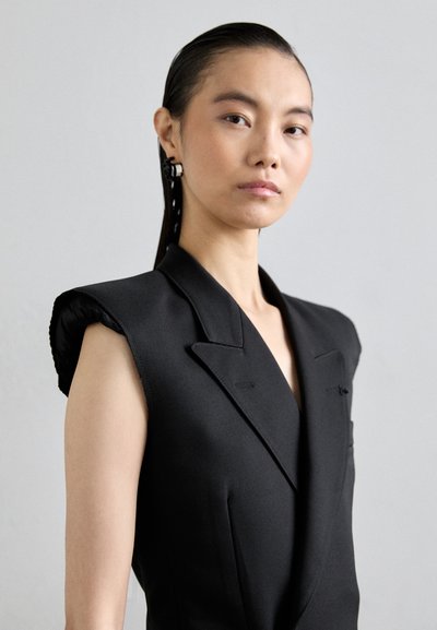 Čierny prispôsobený vest s vystuženými ramenami, s hlbokým V-výstrihom a detailom predného vrecka. Hladká textúra, minimalistický dizajn, bez viditeľných zapínaní.