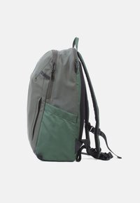 Grüner Rucksack aus glattem, strapazierfähigem Material. Verfügt über mehrere Reißverschlusstaschen, gepolsterte Tragegurte und eine seitliche Mesh-Tasche für zusätzlichen Stauraum.