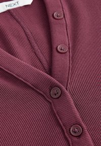 Ribbet bordeaux cardigan med V-hals og fem præget knapper langs frontpladen; blød tekstur med synlige sømme.